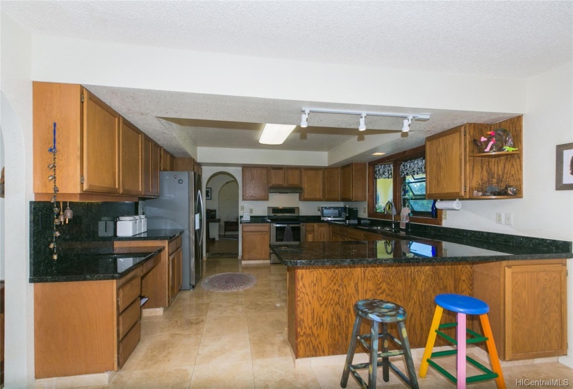 Standing in the family room, the view of the kitchen with so many cabinets to hold all your kitchen dishware and china and gadgets!  Travertine floors and track lighting and look, there's another archway!