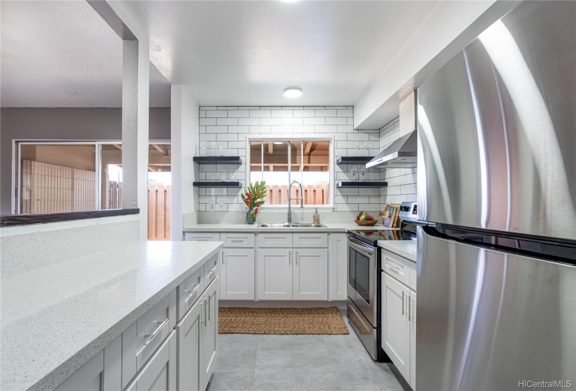 Beautiful kitchen with new flooring, cabinets, counters, shelves, tile backsplash, refrigerator and stove.