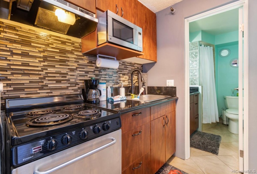 Beautiful kitchen appliances accented with a lovely backsplash, leading to bathroom.