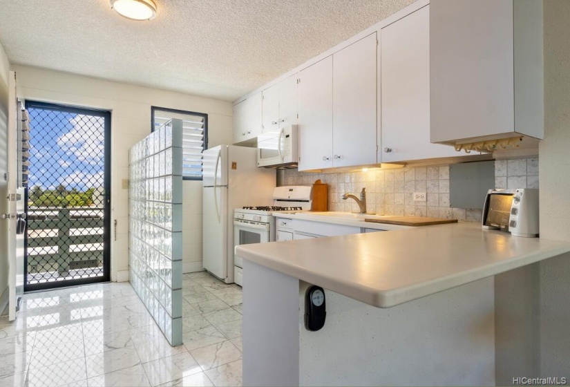 Bright entrance and kitchen with marble tile flooring and backsplash, gas range and ample storage