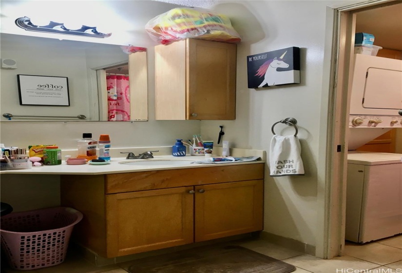 Bathroom Vanity Sink and dressing area has Ceramic Tile Flooring, Built in Cabinetry, Pocket Door leads to W/D area, Full Bathtub/Shower, and Toilet. Vertical view.