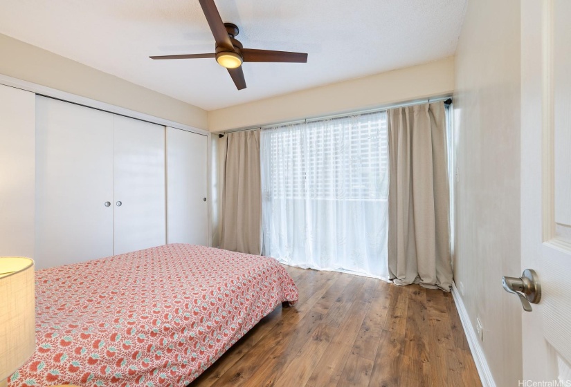 First bedroom with large closet, ceiling fan, window AC, and lanai access.