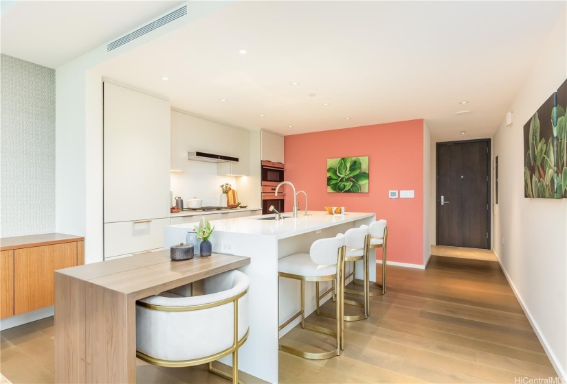 View of the kitchen to the foyer. There's casual counter seating and a table for two that doubles as a work desk.