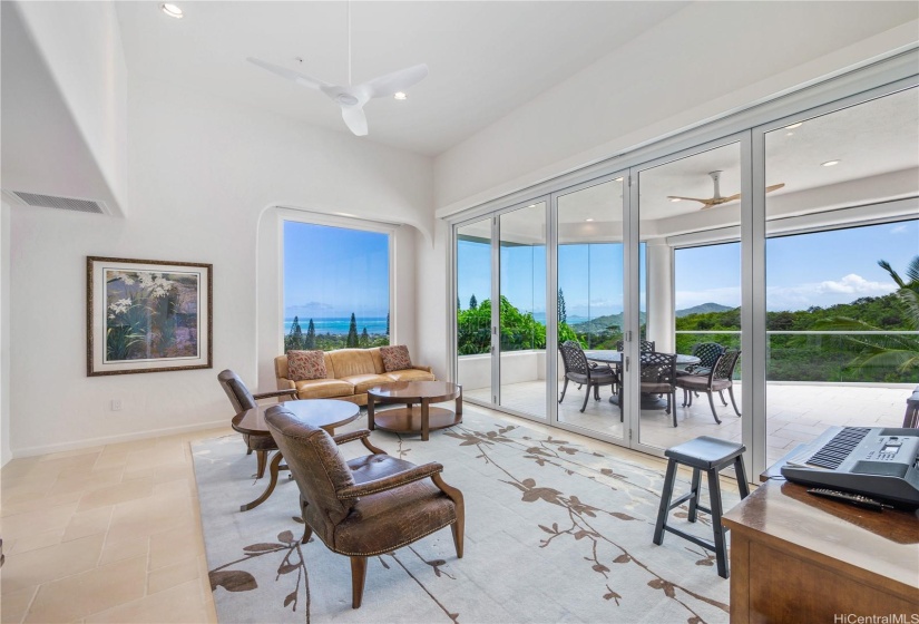 Second living space on the main floor looking out to the lanai dining area, infinity pool, and Pacific Ocean.