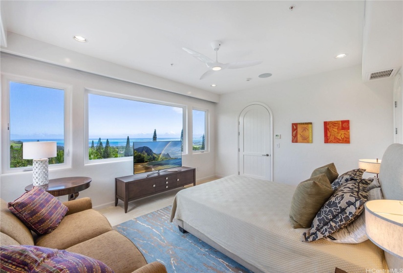 Large, second bedroom on the main floor of the home with views of the Pacific Ocean, high ceilings, large windows, and limestone tile floors.