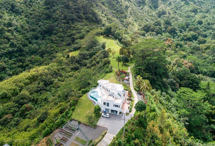 Arial view of the property, raised garden bed areas, lush landscaping, concrete walking path, and private mountain surroundings.