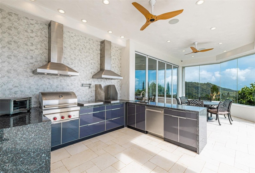 Large outdoor kitchen with extensive cabinet space, grill, pot filler, range, two vent hoods, sink, and dish washer.