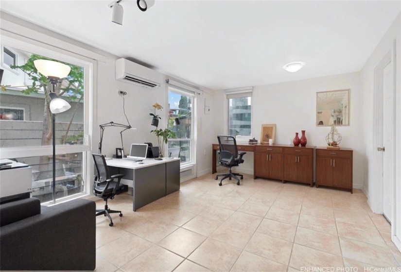 Enhanced photo with virtual staging of another downstairs bedroom that is currently being used as an office. Door to the right leads into a 2 car enclosed garage.