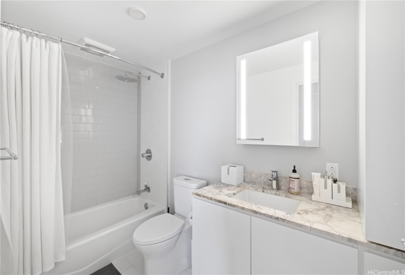 Full bathroom includes a beautiful lighted mirror, storage space, towels and tub.