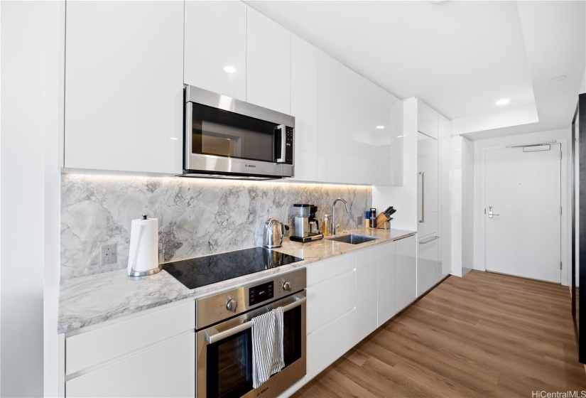 Modern kitchen with backsplash lighting includes coffee machine, paper towel holder, kettle, knives, utensils, and more.