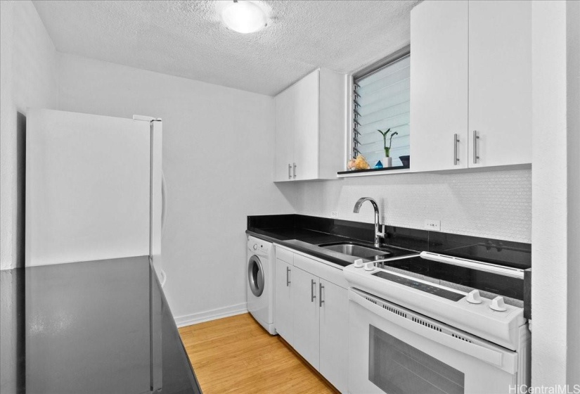 Bright white open kitchen with granite counters, and quality appliances including a Kitchen Aid refrigerator.