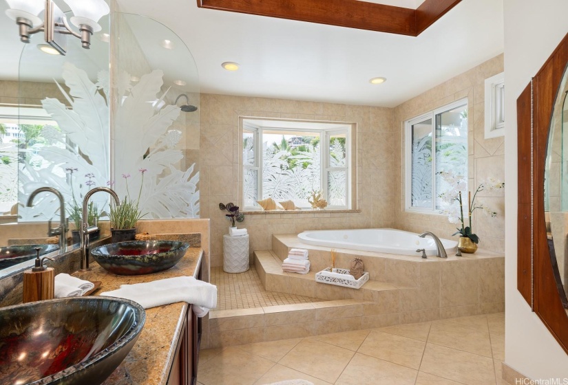 The primary bath features raised ceiling details, a large sit in tub, walk in shower, double vanity with blown glass vessel sinks and etched glass detailing.