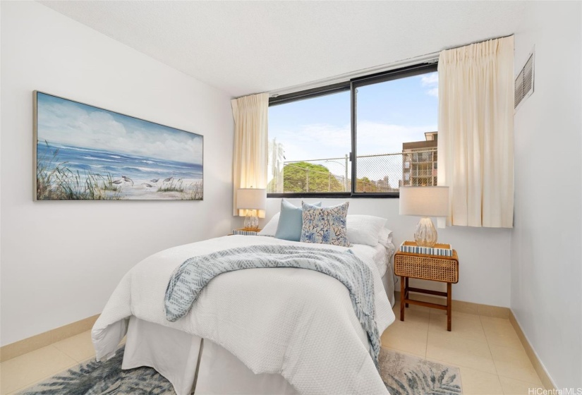 Spacious and bright second bedroom with cool tile flooring and views of the tennis court.