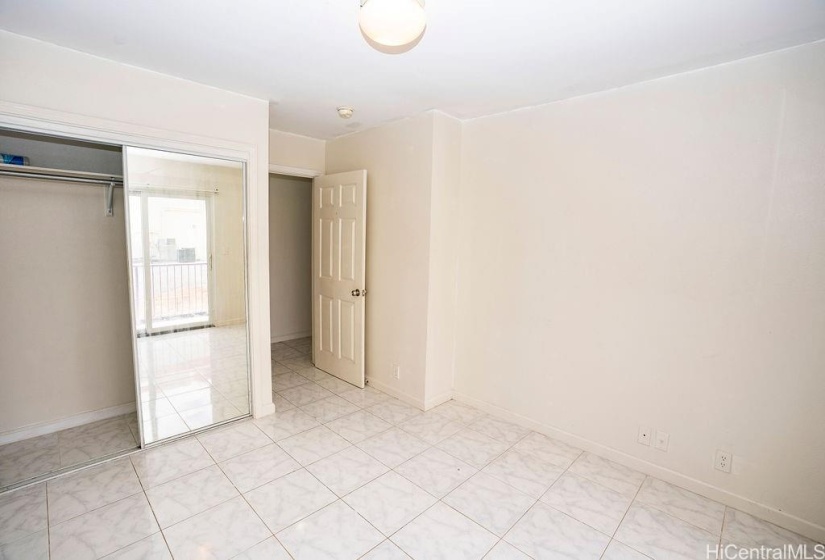 Interior bedroom with mirrored closet doors and tiled floors.