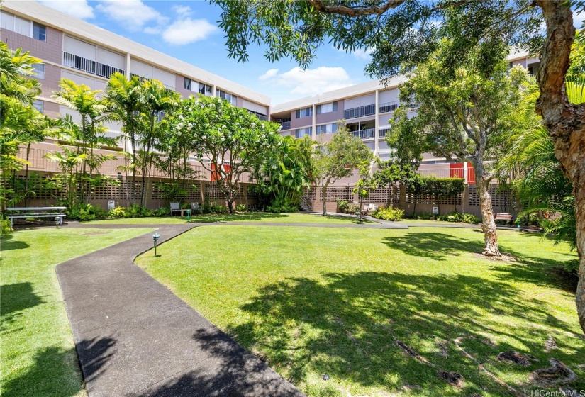 Beautifully landscaped courtyard within the apartment complex. The lush green lawn is meticulously maintained and bordered by a variety of trees and plants, creating a serene and inviting environment.