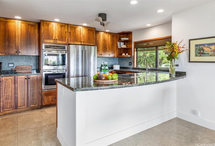 Open kitchen has custom koa cabinets and beautiful granite counters