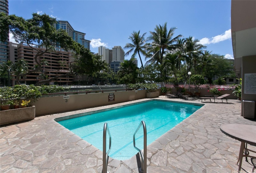 Pool with lounge chairs, round tables in the shade for dining, outdoor relaxation