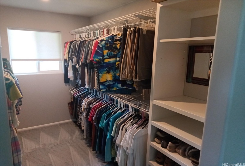 Image of master closet with clothes on right side and built in shoe / storage cabinet.