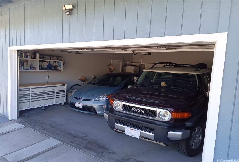 Open garage door with 2 vehicles.