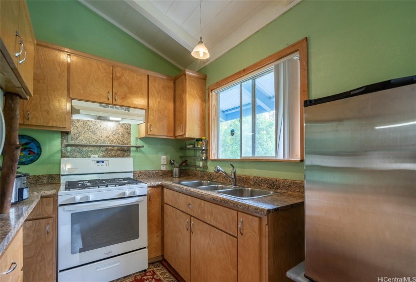 Cute Kitchen with gas range oven, 3 compartment stainless steel sink, built in microwave oven, and stainless steel refrigerator.