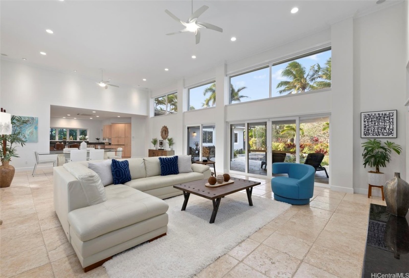 Grand and wide-open living area with 16-foot ceilings, large windows that allow in lots of natural light while framing the palm trees