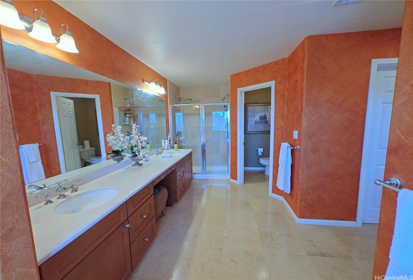 Spacious primary bathroom with double vanity sinks, a seating area, shower, and enclosed toilet area.