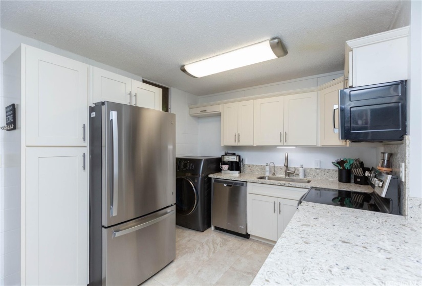 Kitchen has updated quartz counters, ceramic tile, and stainless steel appliances.