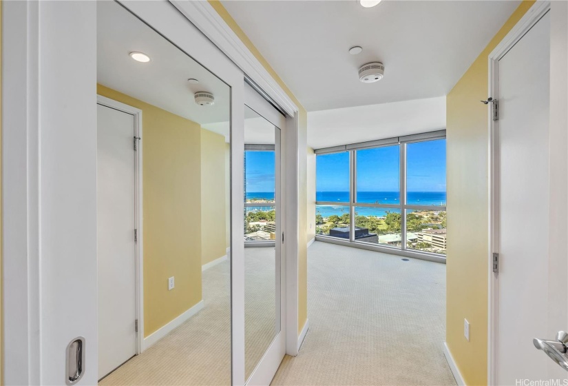 Entry to second bedroom with custom mirrored doors on closet and vibrant ocean view beyond.