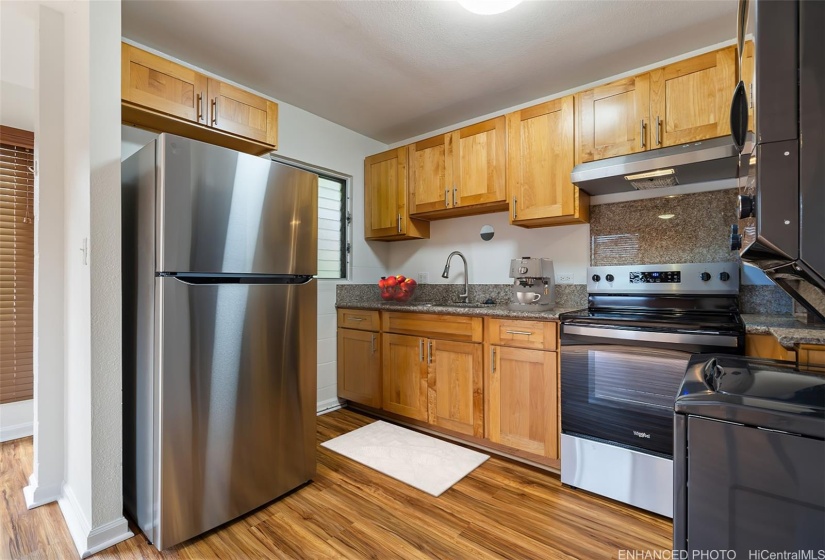 Open kitchen with new refrigerator, recently installed cabinets, range/oven, microwave hood and washer/dryer.  (Enhanced photo)