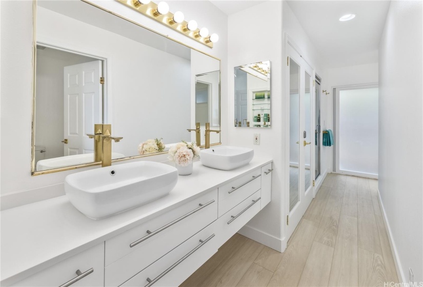 This Primary en-suite bathroom features dual sinks with gold faucets, sleek cabinets, closets, and a European style separate room with tub and shower.