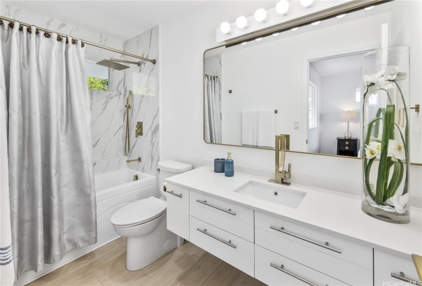 This upstairs new En-Suite Bathroom features shiny sleek cabinets, modern gold faucets and rainforest shower head, and a quartz countertop.