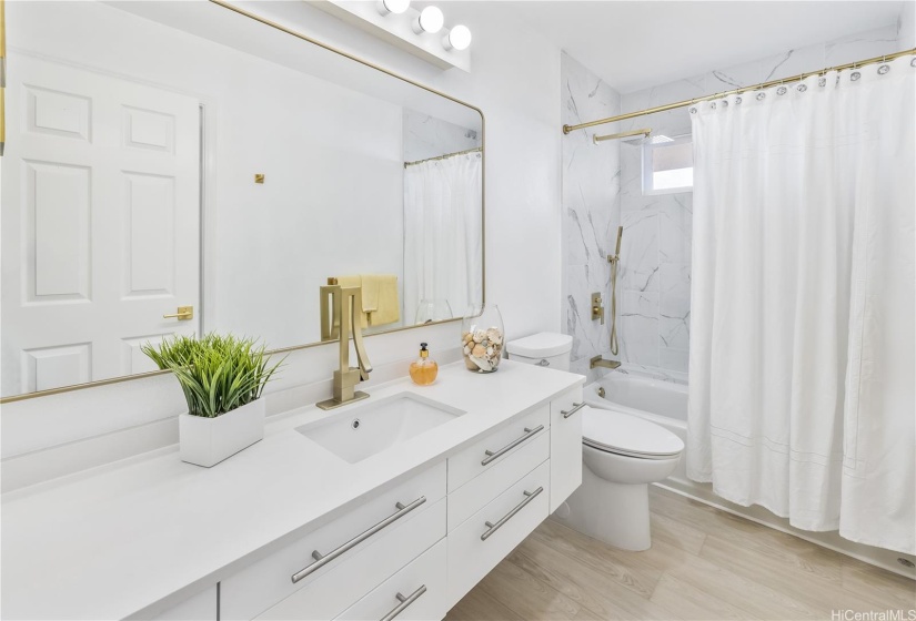 This new upstairs hall bathroom features sleek cabinetry, quartz countertop, and gold faucets for the vanity sink and the shower with a rainforest shower head.
