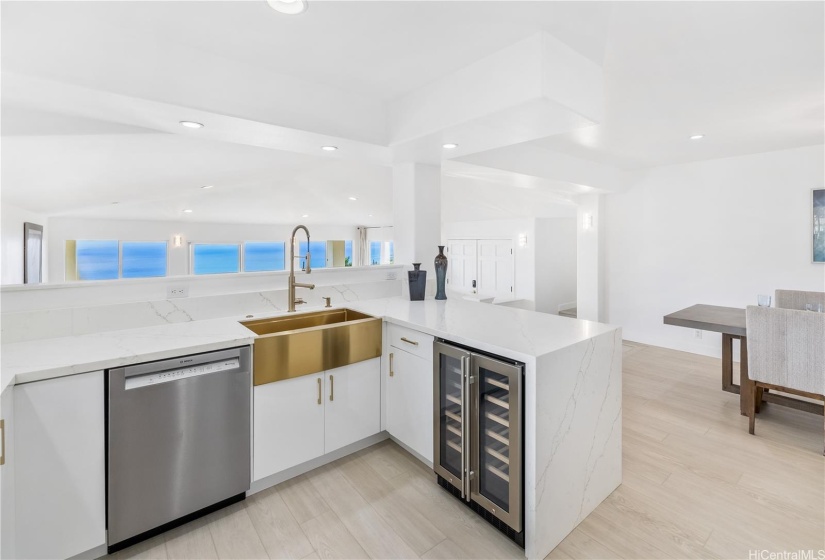 The brand new kitchen with ocean views, sleek white cabinets, quartz countertops, striking gold sinks and fixtures, wine refrigerator, a walk-in pantry, and all new Bosch appliances, opens to the dining and living areas for easy gatherings of friends and family.
