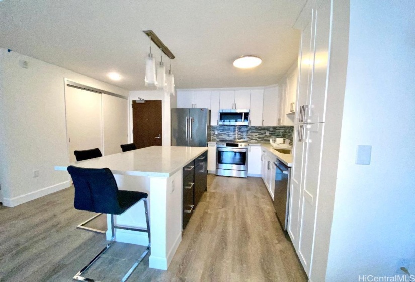 A view of the modern kitchen and island toward the entry.  The stacked washer and dryer and water heater are in the closet just inside the entry.