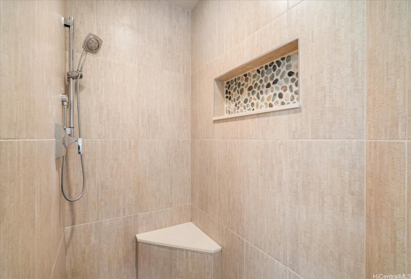 The primary walk-in shower is beautifully finished with porcelain tile and river rock accents.